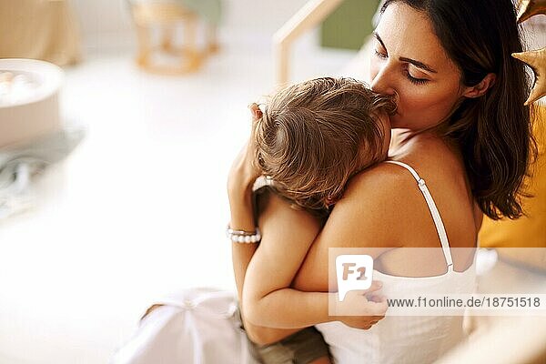 Junge Frau Mutter drückt Liebe zu kleinen Baby  sitzt auf dem Bett mit schlafenden Kind in den Händen und küsst es in die Stirn  zarte Foto der bedingungslosen Liebe zwischen Mutter und Sohn