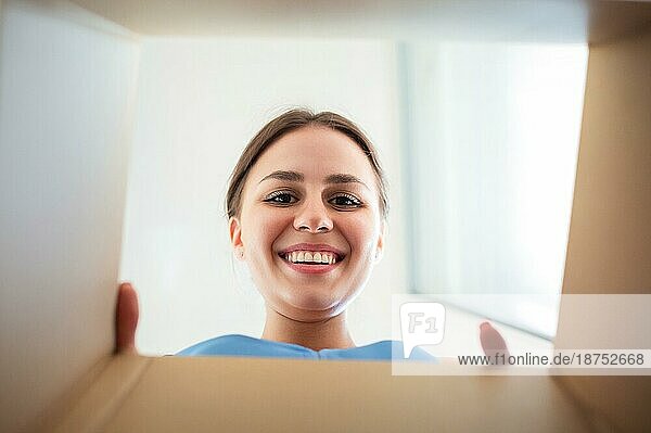 Von unten glückliche junge Frau  die lächelnd in den Karton schaut  während sie die bestellte Ware öffnet