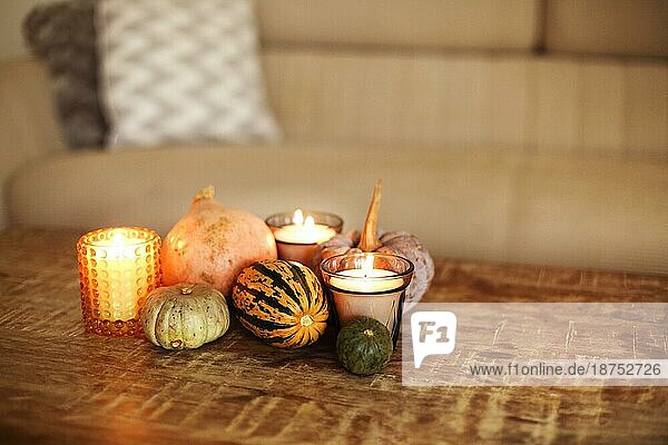 Rustikalen Stil hölzernen Couchtisch im Wohnzimmer Interieur Hintergrund  mit kleinen dekorativen bunten Kürbisse und drei brennende Kerzen verschönert. Herbstferien  Thanksgiving oder Halloween Konzept