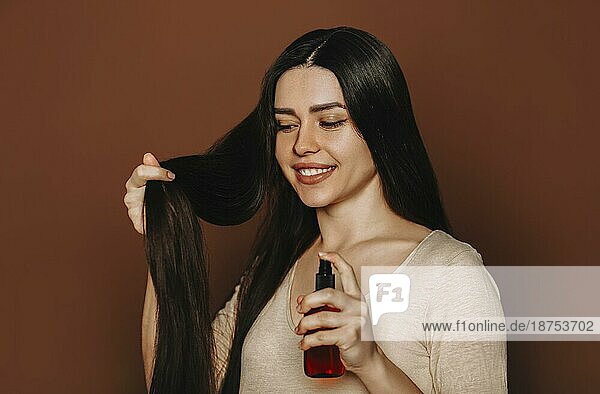 Studioporträt einer glücklichen  zufriedenen Frau  die ihr langes  gesundes  braunes Haar hält und in die Kamera zeigt  daß sie Shampoo oder Spülung benutzt  eine Frau  die natürliche  parabenfreie Haarpflegeprodukte verwendet  selektiver Fokus