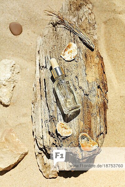 Draufsicht auf eine Flasche mit aromatischem ätherischem Öl  die auf rauem Holz in der Nähe von Steinen und Zweigen am Sandstrand steht