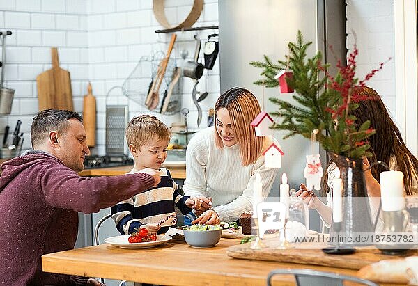 Liebender Mann und liebevolle Frau mit kleinem Jungen und Schwester am Tisch  die zusammen essen und die Weihnachtsferien genießen
