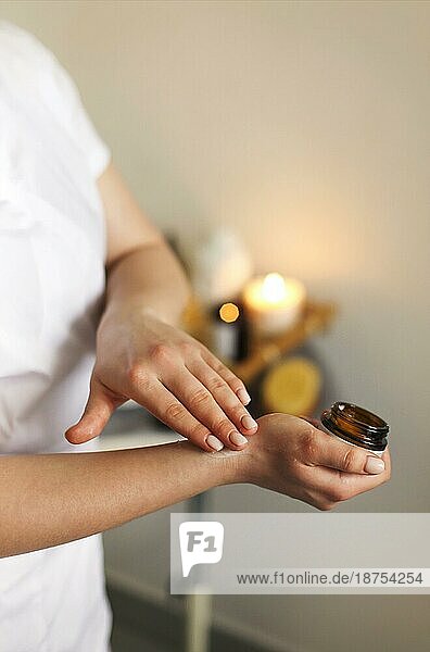 Junge Kosmetikerin trägt vor der Behandlung im Salon Creme aus einem Tiegel auf die Hand auf