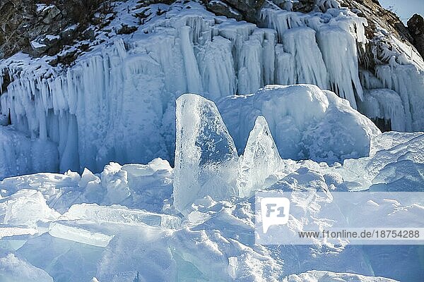 Eiswürfel auf dem idealen glatten Eis des Baikalsees mit Eishügeln am Horizont. Die Sonne scheint durch die Seiten der Eiswürfel. Die Schollen sehen aus wie Diamanten
