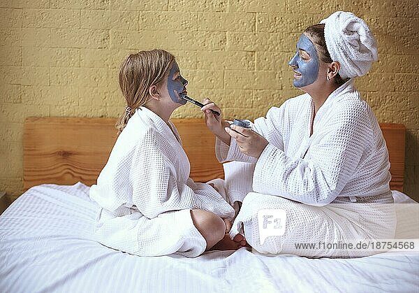 Glückliche Familie Mutter und Baby Tochter machen Gesichtsmaske  Hautpflege zusammen
