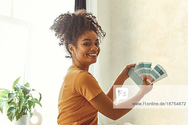 Lächelndes afroamerikanisches Mädchen steht mit dem Rücken zur Kamera in der Mitte eines Schlafzimmers mit einer Palette von Blautönen für die Innenrenovierung  die Wahl der Farbe für das Gleichgewicht von Geist und Körper  erfrischendes Innendesign