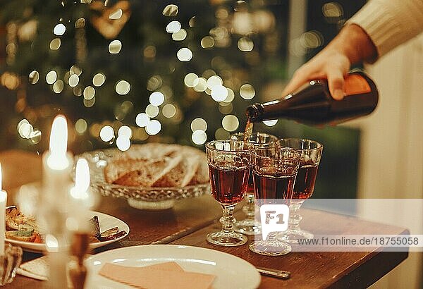 Silvesterfeier. Mann gießt Champagner in Gläser stehen auf dem Tisch mit festlichen Weihnachtsessen  Kerzen und eingepackt Geschenke gegen unscharfen Hintergrund und firtree  beschnitten