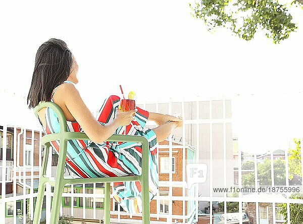 Niedriger Winkel Seitenansicht von unerkennbaren weiblichen Ruhe auf Stuhl auf dem Balkon beim Genießen frischen Aperol und beobachten Straße im Sommer