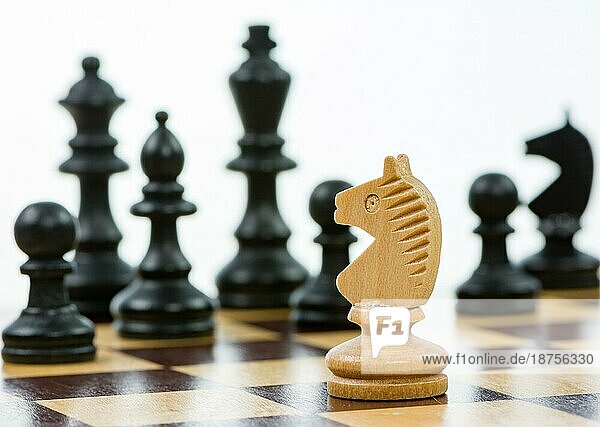 Weißer Springer gegen eine Übermacht von schwarzen Schachfiguren auf einem Schachbrett. Selektiver Fokus