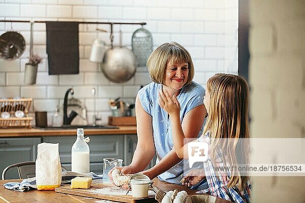 Glückliche erwachsene reife Frau kocht zusammen mit niedlichen kleinen Mädchen am Tisch in der Küche