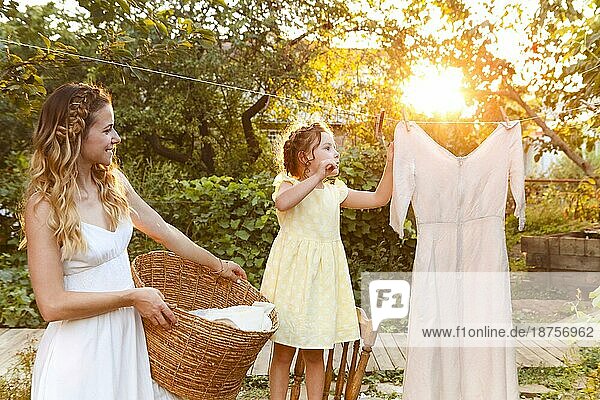Charmantes kleines Mädchen  das seiner Mutter mit einem Weidenkorb hilft  während es die Wäsche im Garten im Sommer aufhängt