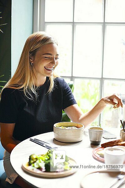 Glückliche junge Frau mit einer Tasse frischen Kaffees  die lächelnd am Tisch im Restaurant sitzt