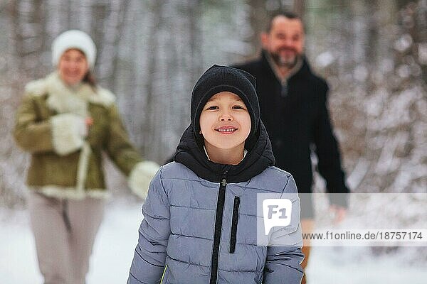 Fröhliche Eltern  die hinter einem fröhlichen Jungen mit Schlitten gehen  während sie an einem Wintertag Zeit im verschneiten Wald verbringen