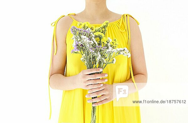 Unerkennbare Frau in gelbem Kleid versteckt sich hinter einem Strauß Wildblumen an einem Sommertag vor weißem Hintergrund