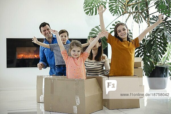 Glückliche Familie sitzt auf dem Boden im Wohnzimmer. Lustige Kinder springen aus Karton Box  Eltern lachen  spielen mit Kindern Spaß haben zusammen in ein neues Haus zu bewegen. Hypothekendarlehen und verlagern Konzept