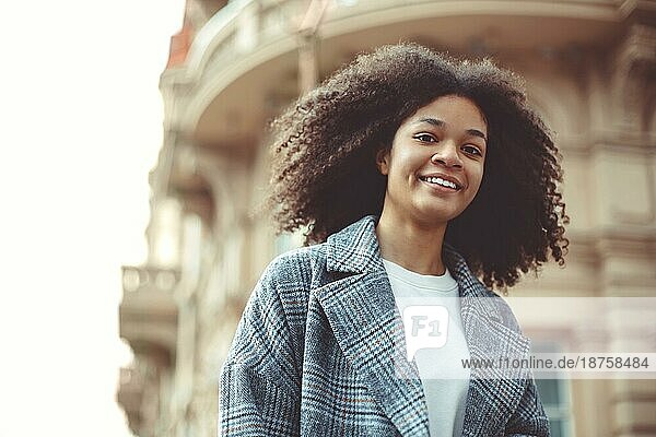 Junge stilvolle positive afroamerikanische Frau überqueren Zebrastreifen und lächelnd in die Kamera beim Gehen in der Stadt auf Herbsttag. Glückliches schwarzes Mädchen auf dem Zebrastreifen im Freien. Menschen auf den Straßen der Stadt