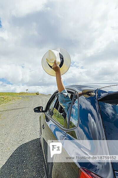 Weibliche Hand hält Hut aus dem Autofenster