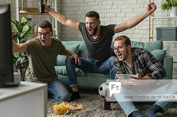 Vorderansicht fröhliche männliche Freunde  die zusammen Sportfernsehen schauen  während sie Snacks und Bier trinken. Foto mit hoher Auflösung