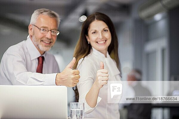 Lächelnde erfolgreiche Geschäftsleute mit Daumen nach oben Zeichen Büro