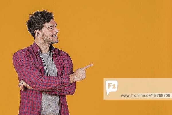 Lächelndes Porträt eines jungen Mannes  der mit dem Finger auf einen orangefarbenen Hintergrund zeigt