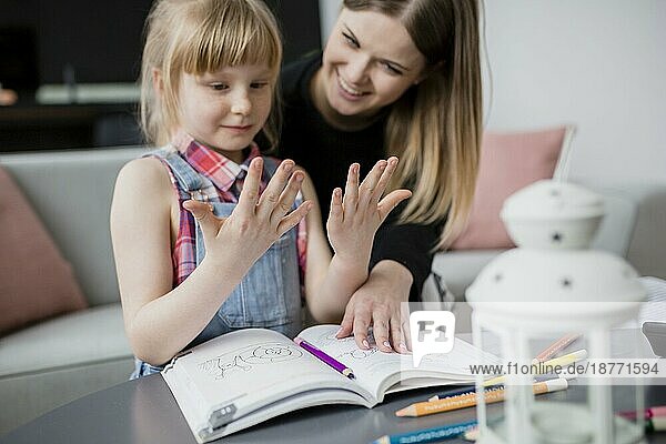 Mädchen  das sich die Hände hält  während es mit seiner Mutter Hausaufgaben macht