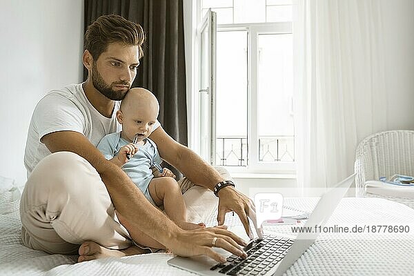 Vater  der während der Quarantäne mit seinem Kind zu Hause am Laptop arbeitet. Foto mit hoher Auflösung