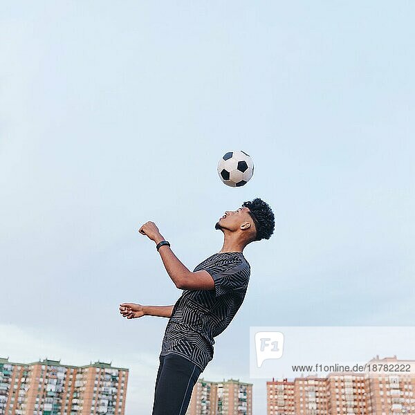 Männlicher Sportler beim Training mit Fußball vor blauem Himmel