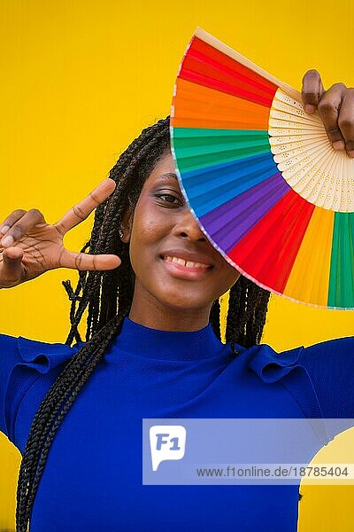 Eine schwarze ethnische Frau mit einem Regenbogen lgbt Fan auf einem gelben Hintergrund  so dass der Sieg Symbol