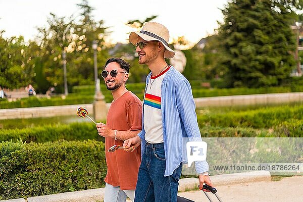 Männliche Touristen Homosexuell Freunde mit einem Koffer in den Park bei Sonnenuntergang in der Stadt den Besuch der Stadt für den Stolz Festival. lgbt Konzept