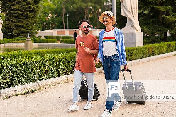 Männliche Touristen Homosexuell Freunde mit einem Koffer in den Park bei Sonnenuntergang in der Stadt den Besuch der Stadt für den Stolz Festival. lgbt Konzept
