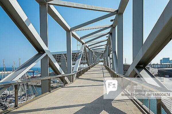 Eine industrieästhetische Fußgänger Fachwerkbrücke führt über den Yachthafen Port Forum in Barcelona. Das riesige Solarpanel ist ein Wahrzeichen des Hafens