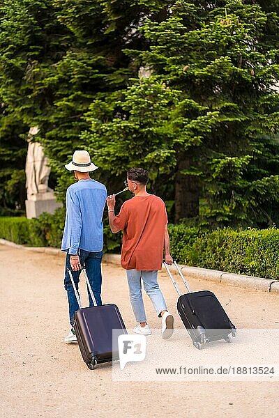 Männliche Touristen Homosexuell Freunde Rücken an Rücken mit einem Koffer im Park bei Sonnenuntergang in der Stadt den Besuch der Stadt für den Stolz Festival. lgbt Konzept