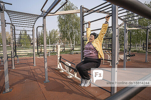 Senior woman hanging on exercise equipment at park