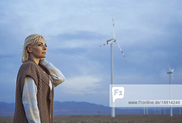 Blond woman with hand in hair standing near wind turbines in desert
