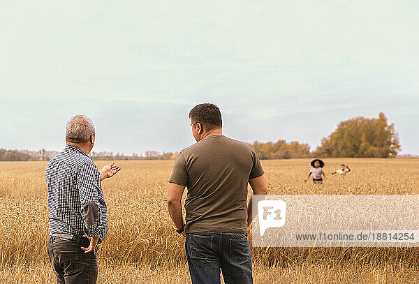 Father and son standing in field and children playing in background