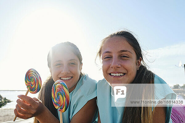 Smiling twin sisters holding lollipop candy at beach