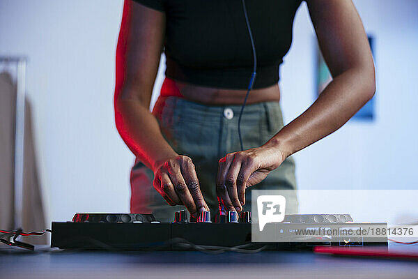 Young female Dj operating sound mixer at home
