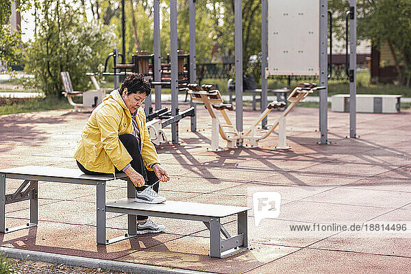 Senior woman tying shoelace sitting on bench at park