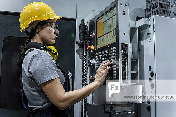 Maintenance engineer wearing hardhat operating machine keypad in modern factory