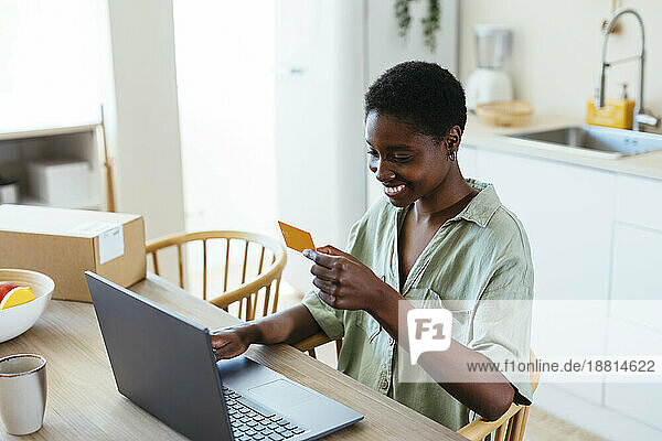 Glückliche Frau  die zu Hause per Kreditkarte auf dem Laptop bezahlt