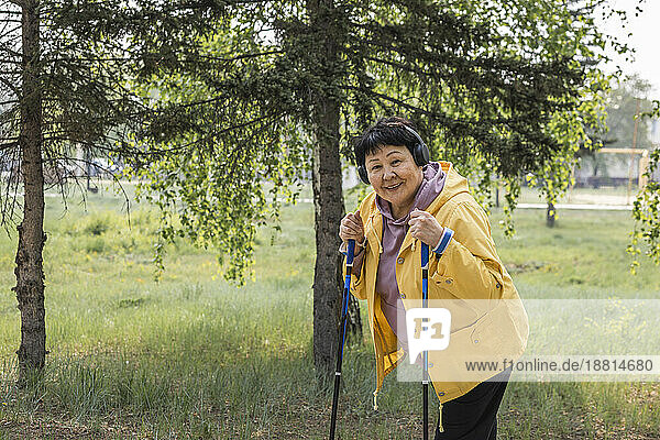 Lächelnde ältere Frau hält Spazierstöcke im Park