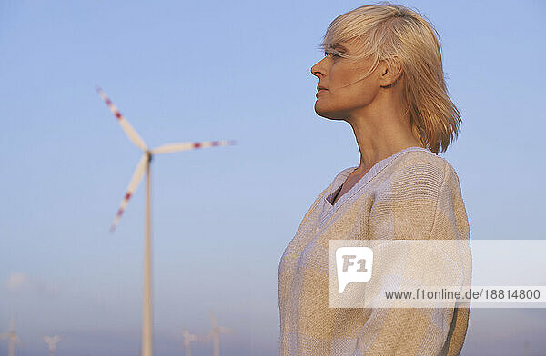 Contemplative woman standing near wind turbine in desert