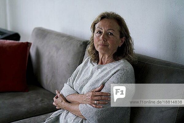 Senior woman sitting with arms crossed on sofa at home