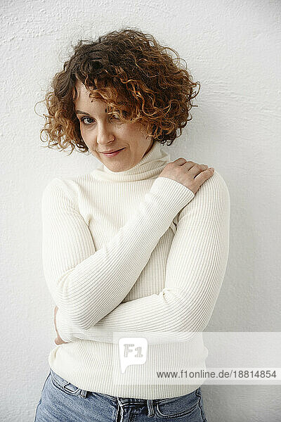 Woman with hand on shoulder standing in front of white wall