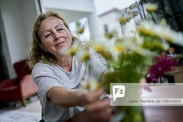 Smiling senior woman touching flowers at home