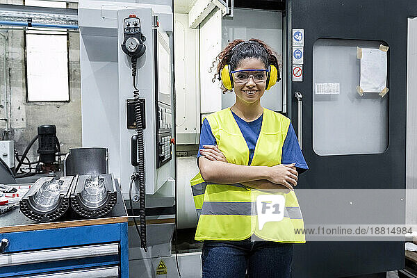Maintenance engineer in reflective clothing standing with arms crossed in modern factory