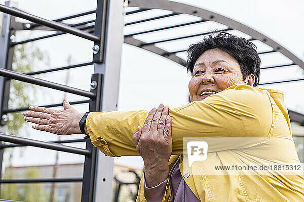 Lächelnde ältere Frau macht Aufwärmübung im Park