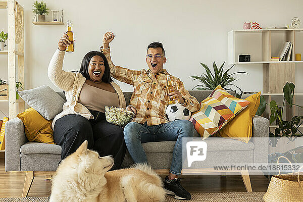 Cheerful couple watching TV and enjoying beer at home