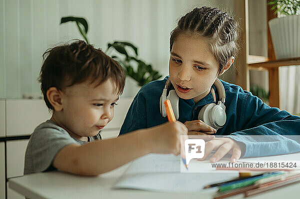 Brother teaching sibling to draw on paper at home
