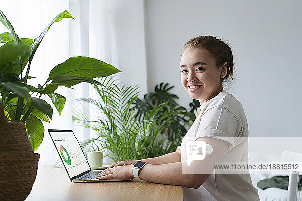 Lächelnde Frau  die an Diabetes leidet  sitzt zu Hause mit Laptop auf dem Tisch